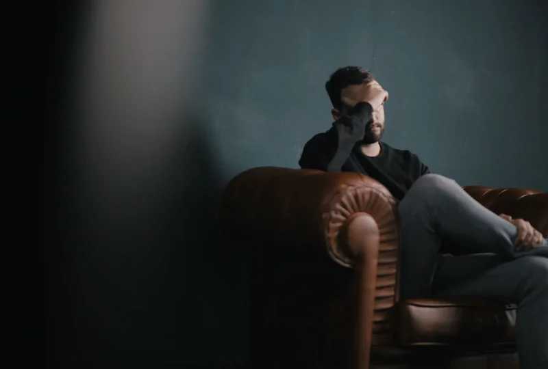 A man sitting on a couch with his hand over his face, struggling with a mood disorder.
