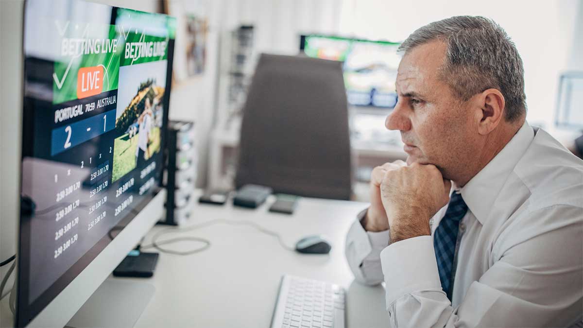 A man in a white shirt intently watches a computer screen displaying live betting odds for a Portugal vs. Australia match