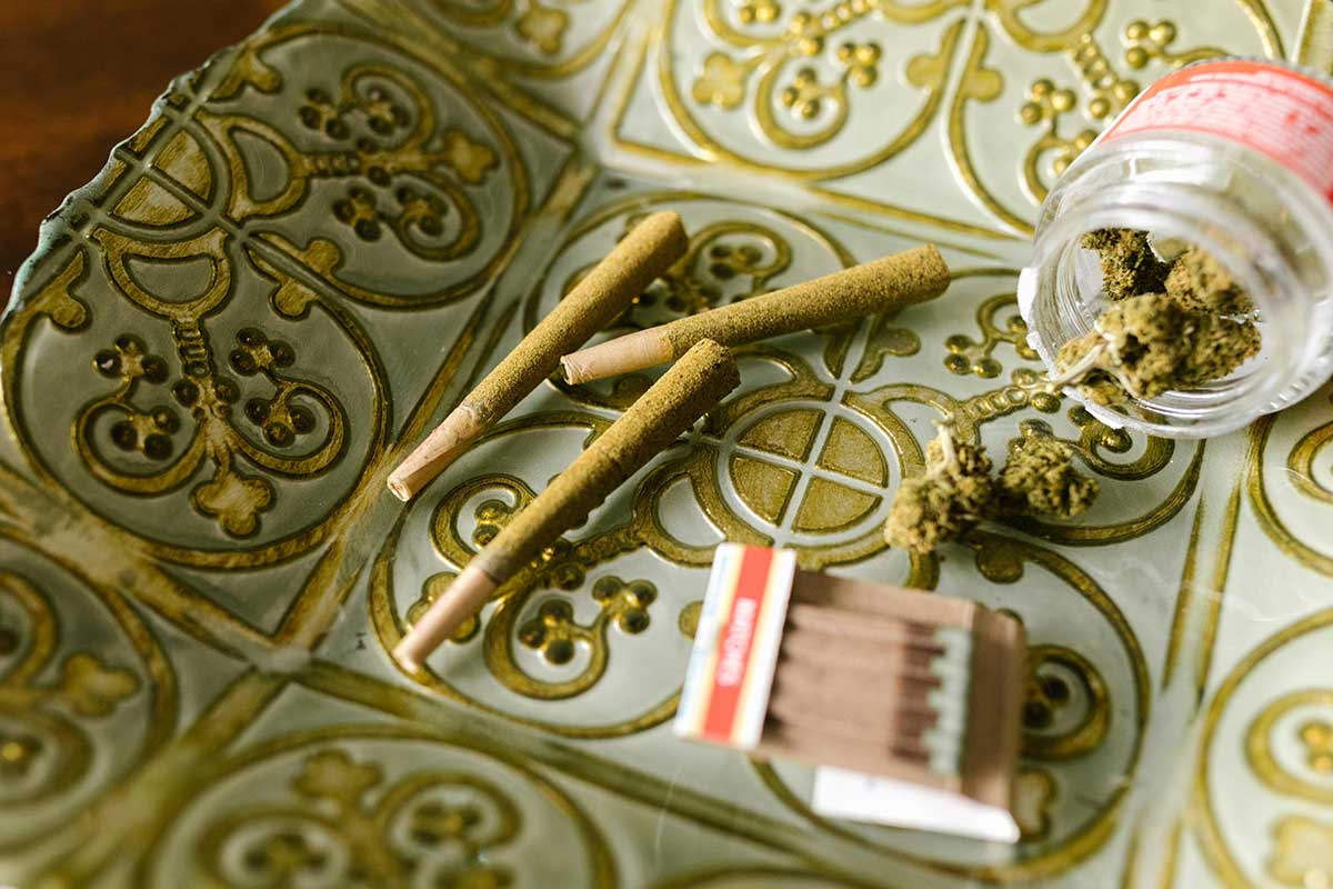 Items linked to marijuana addiction: pre-rolled joints, a matchbox, and loose buds on a decorative tray.