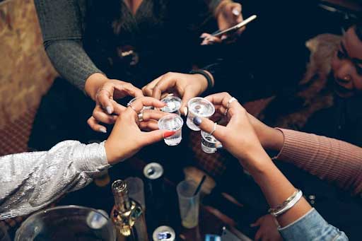 Group of friends toasting with shots of clear liquor at a cozy indoor gathering.
