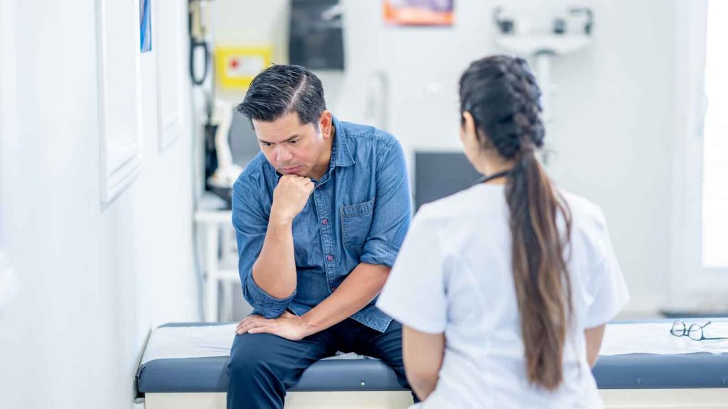 Man sitting on exam table looking concerned with a doctor.