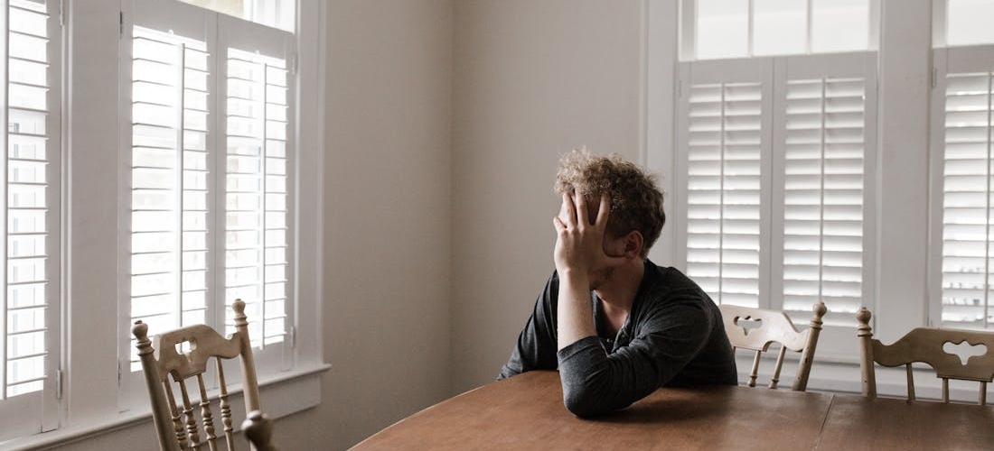 A person sitting alone at a wooden table, showing stress related to anxiety and alcohol